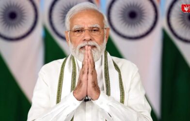 An Indian political leader standing with folded hands in front of national flags during an official event
