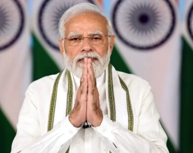 An Indian political leader standing with folded hands in front of national flags during an official event