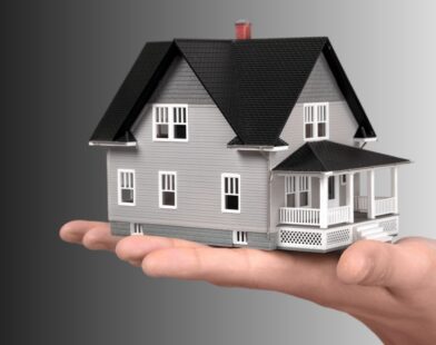 A hand holding a small house model with a bank loan approval symbol, representing financial support for home reconstruction