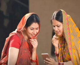 Two rural women smiling while checking scheme benefits on a mobile phone under the Ladki Bahin Yojana