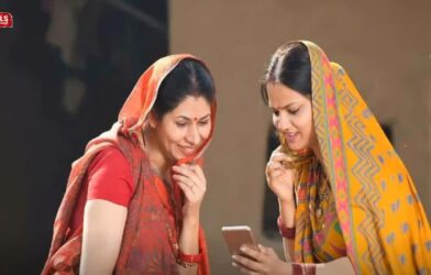 Two rural women smiling while checking scheme benefits on a mobile phone under the Ladki Bahin Yojana