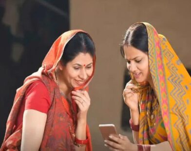 Two rural women smiling while checking scheme benefits on a mobile phone under the Ladki Bahin Yojana