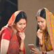Two rural women smiling while checking scheme benefits on a mobile phone under the Ladki Bahin Yojana