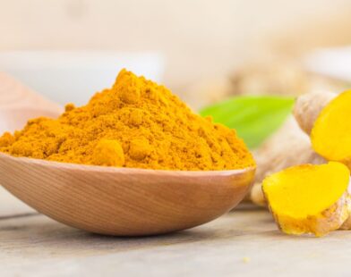 A bowl of turmeric powder with fresh turmeric roots placed beside it, highlighting the risks of excess turmeric consumption for kidney and liver health